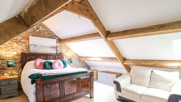 A bedroom with a wooden bed, a white sofa, and a stone wall. - The Bake House (Bridgend)