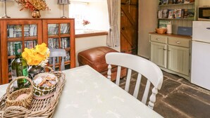 A cozy kitchen with a dining table, a wicker basket with pastries, a vase with flowers, and a bookshelf filled with books. - The Bake House (Bridgend)