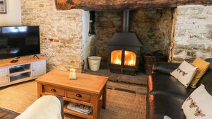 A cozy living room with a stone wall, a wooden coffee table, a leather sofa, and a fireplace with a visible fire. - The Bake House (Bridgend)