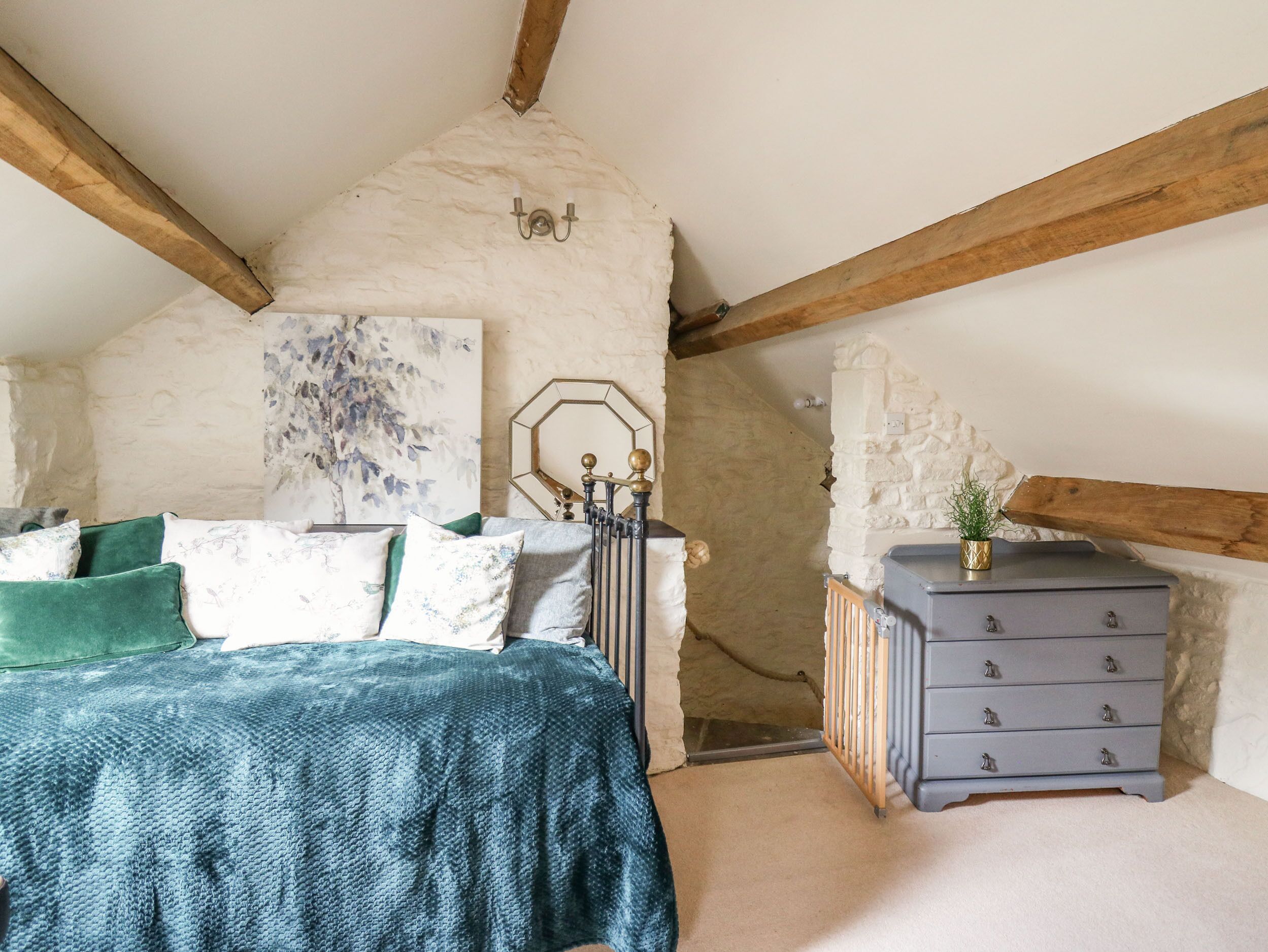 A bedroom with a sloped ceiling, exposed wooden beams, a bed with green and white bedding, a dresser, and a radiator.