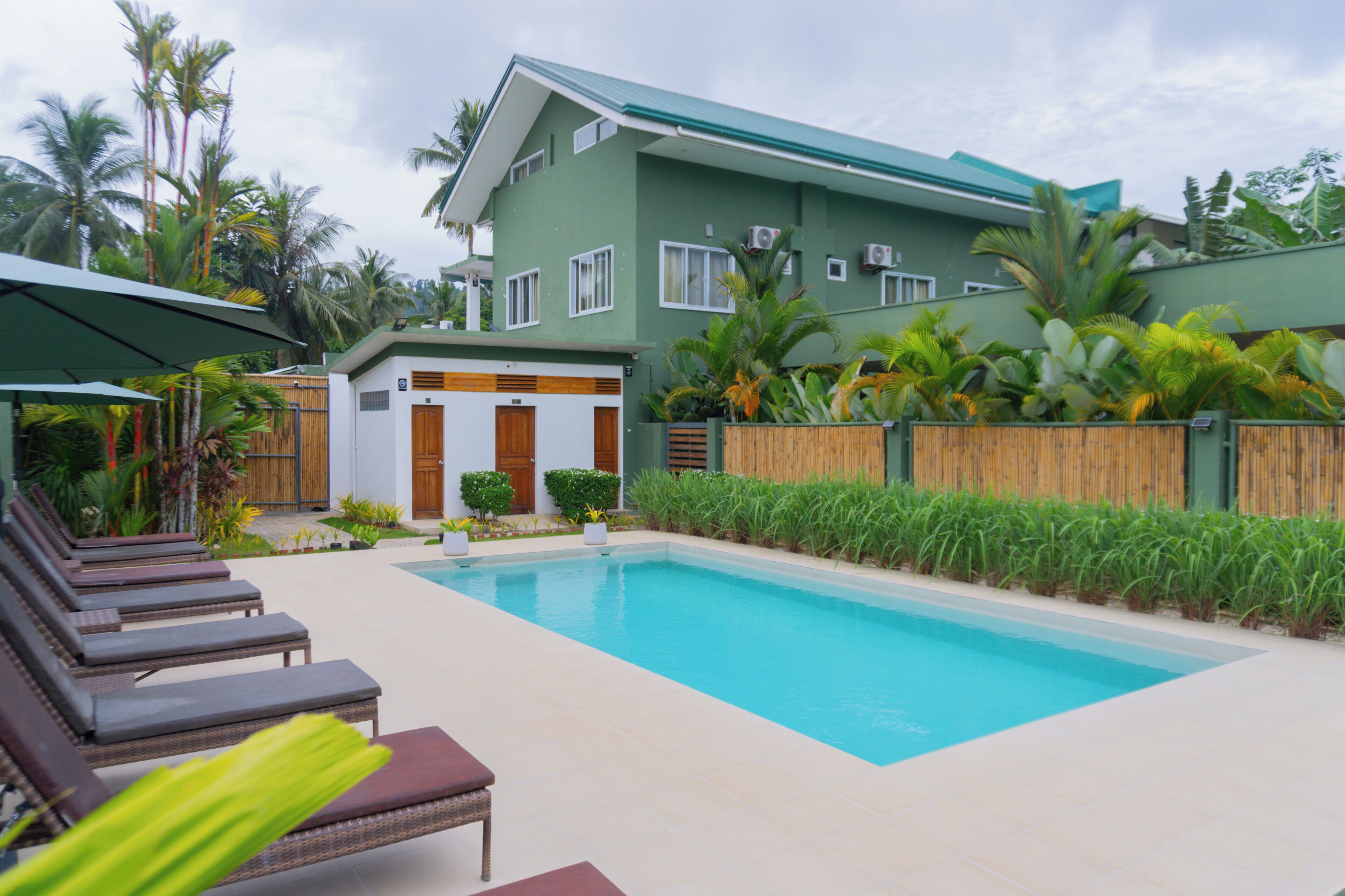 A swimming pool with lounge chairs, a wooden fence, and tropical plants.