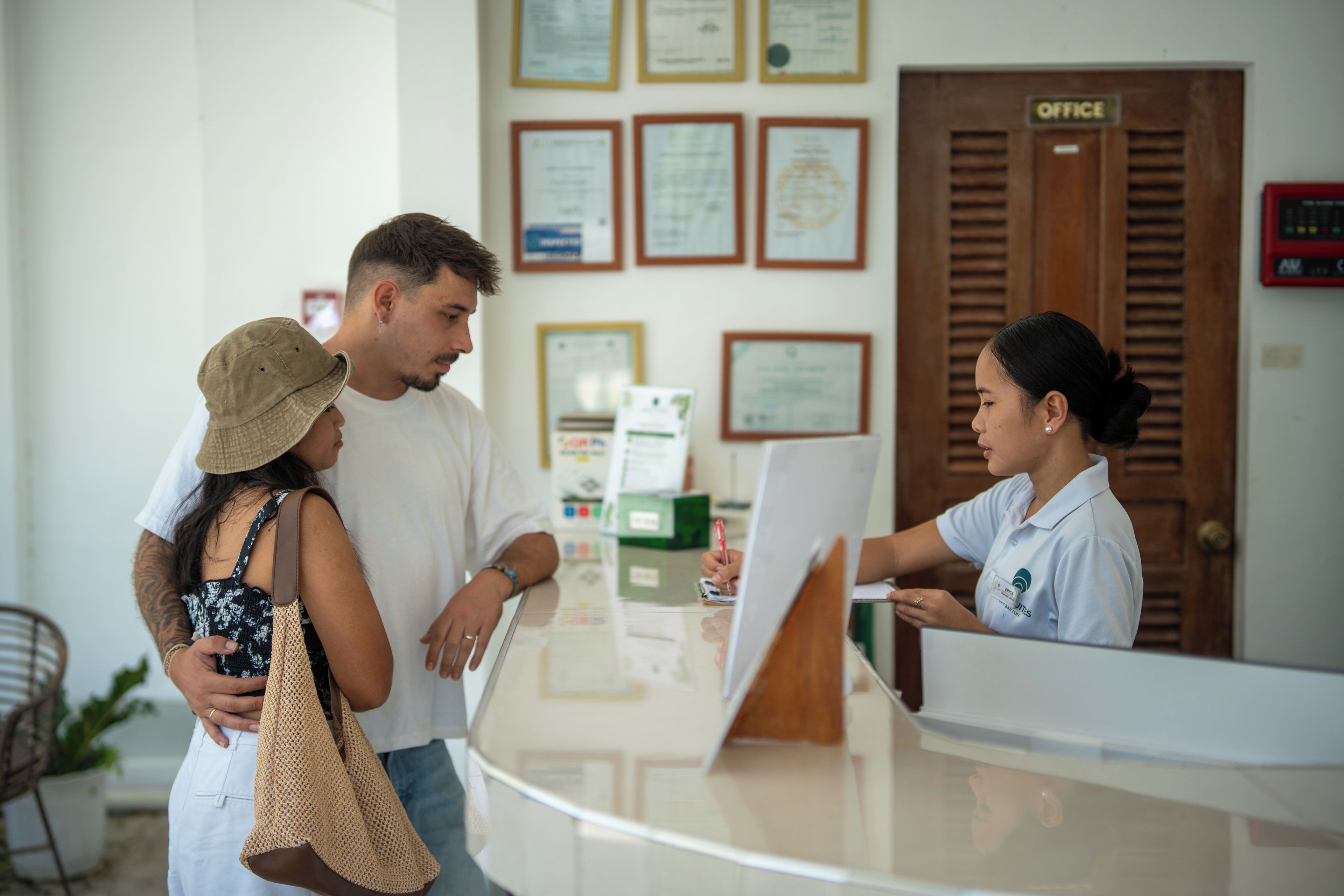 A reception desk with a receptionist, a man and a woman standing in front of it.