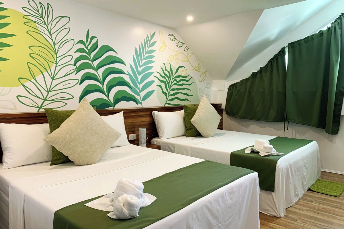Een hotelkamer met twee bedden, groene spreiën, witte kussens en een wanddecoratie met bladmotieven.