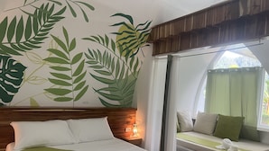 Een hotelkamer met een bed, een zithoek met uitzicht en een wand met bladmotief.