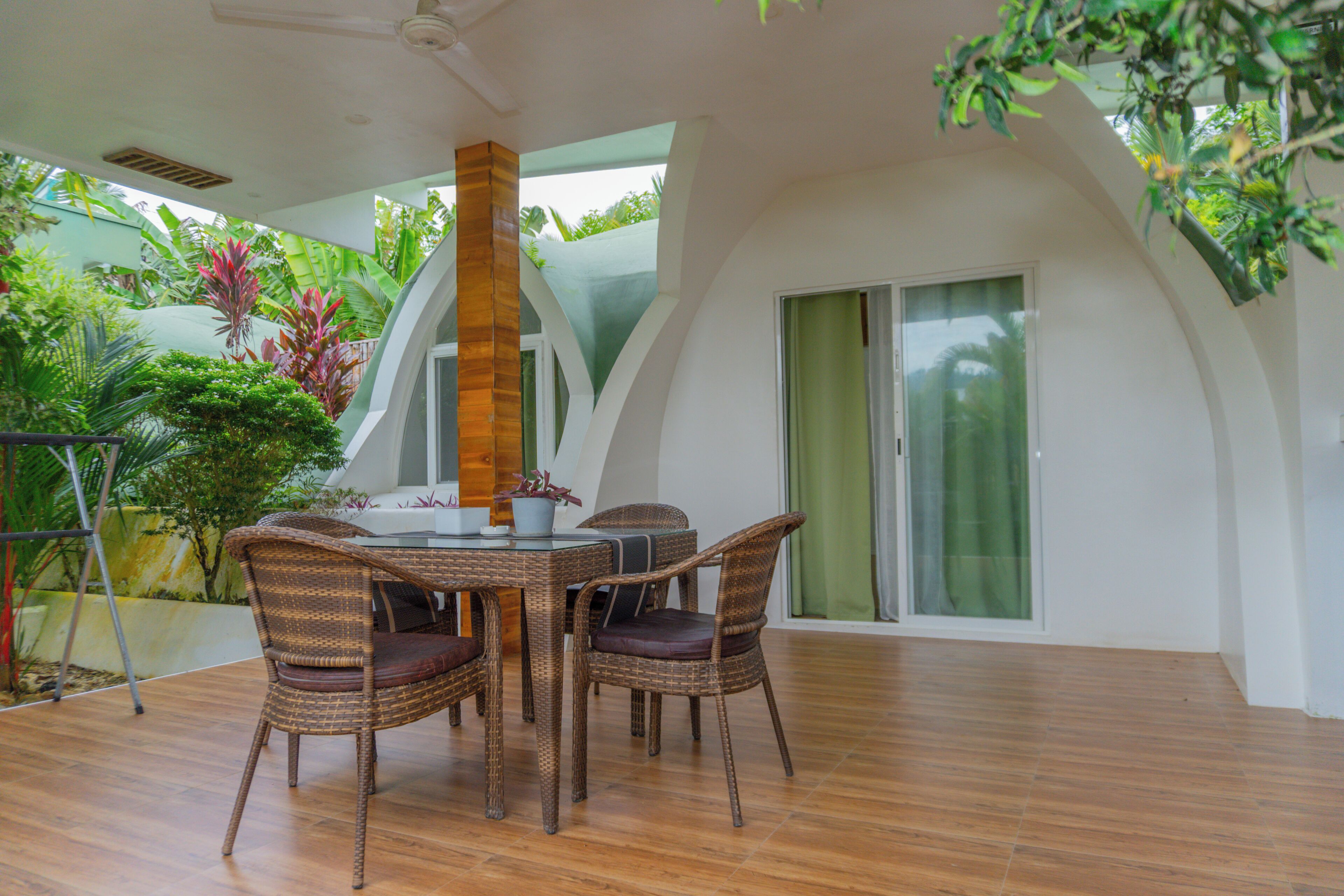 A dining area with a round table and wicker chairs, surrounded by a wooden floor and a view of greenery.