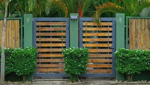 Een omheind toegangspunt met een houten hek en een groene poort, omringd door kleine struiken met witte bloemen.
