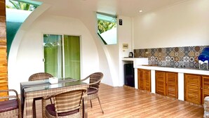 Een moderne keuken met een betegelde spatwand, houten kastjes en een eethoek met rieten stoelen en een glazen tafel.