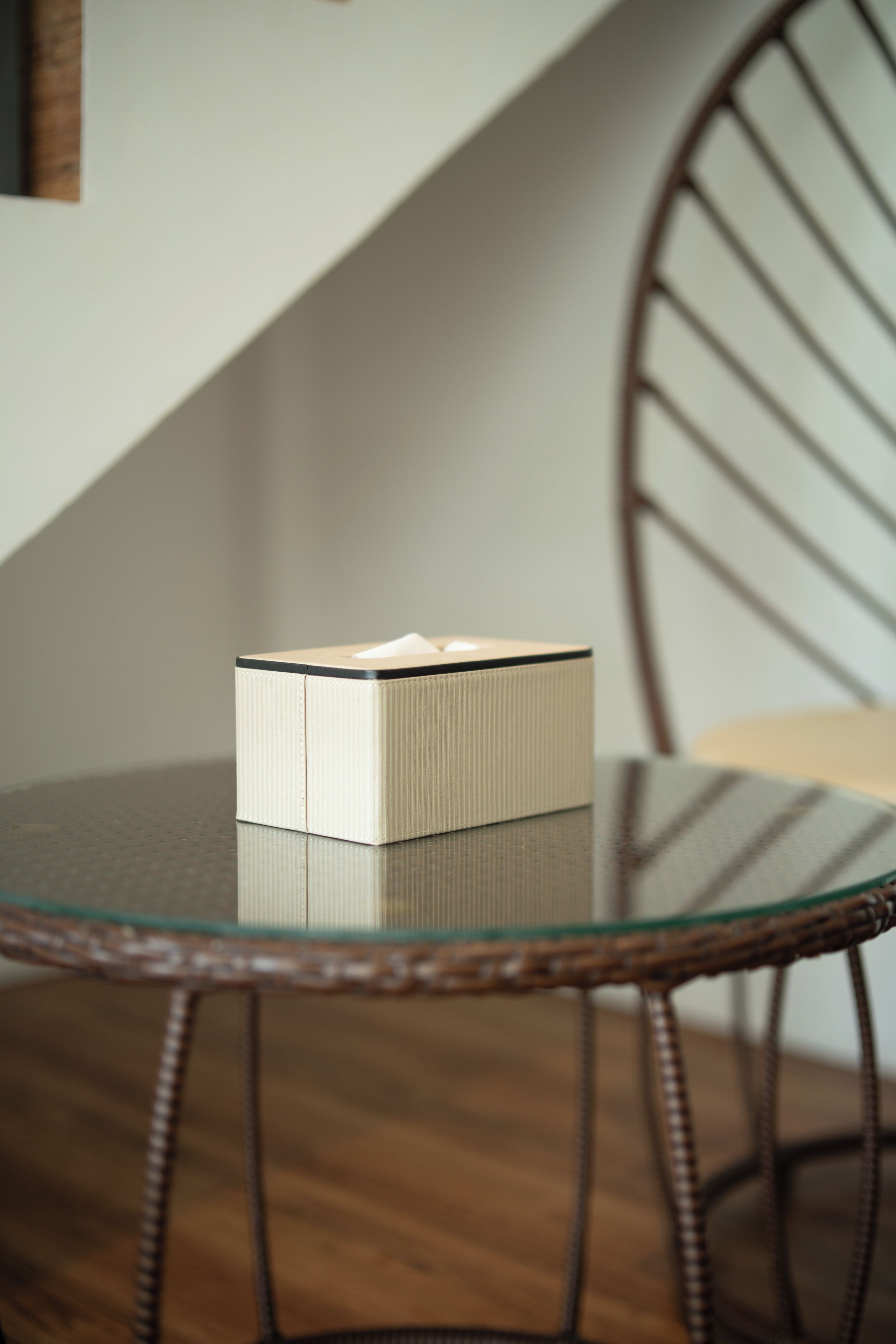 A white box on a glass table with a woven chair in the background.