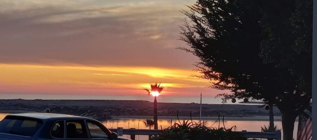 A sunset over a body of water with a car and a street lamp in the foreground.