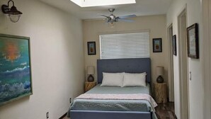 Een slaapkamer met een bed, plafondventilator, wandlamp en ingelijste foto's.