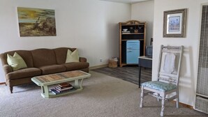 Una sala de estar con un sofá marrón, una mesita de centro verde con libros, un mueble azul y una silla blanca.
