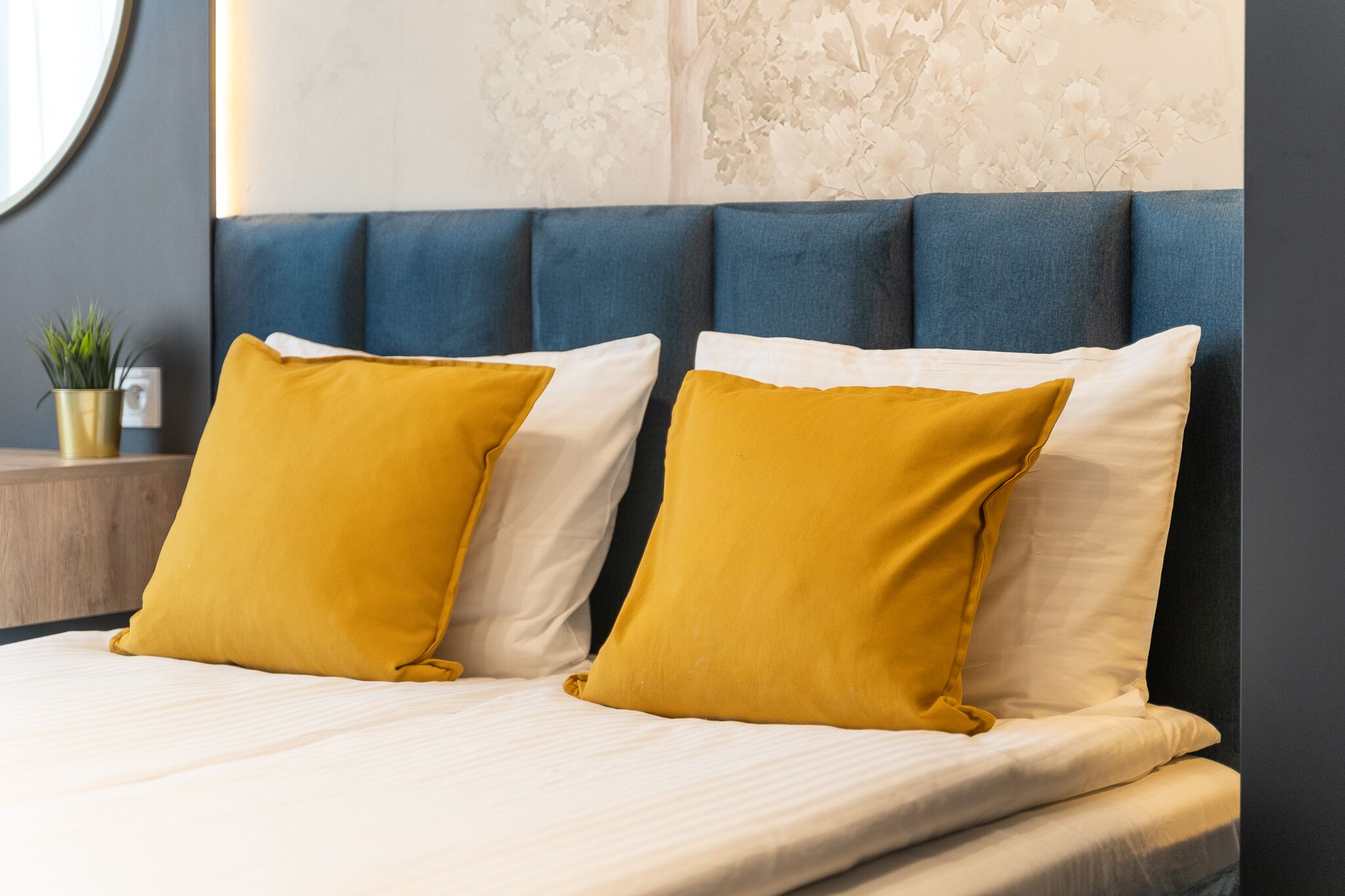 Een bed met een blauw hoofdeinde en twee mosterdgele kussens.