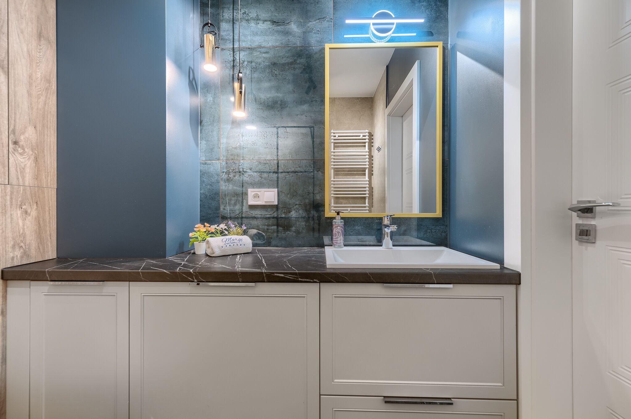 Une salle de bain avec un plan de toilette en marbre, un lavabo blanc, un miroir avec un cadre doré et un porte-serviettes.