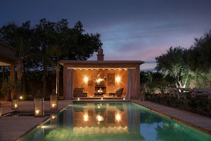 Zona junto a la piscina con mobiliario, chimenea e iluminación ambiental.