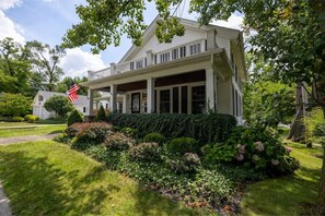 Stunning two-story home with a charming front porch and balcony, set amidst a beautifully maintained garden and lush trees.