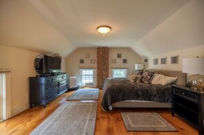Cozy bedroom with a large bed, dresser, and TV, set against a brick accent wall.