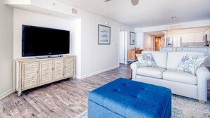 Una sala de estar moderna con una televisión de pantalla plana, un sofá blanco y un reposapiés azul.