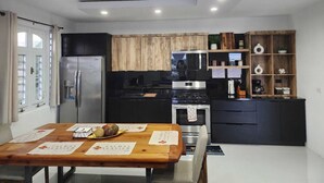 A modern kitchen with a stainless steel refrigerator, a microwave, and a stove. There is a wooden dining table with placemats and a bowl of fruit.