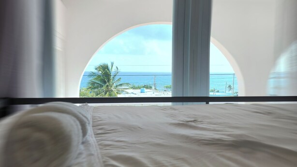 A bed with a view of the ocean through a large window.