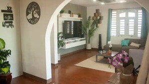 A modern living room with a flat-screen TV, a sofa, a coffee table, and potted plants.