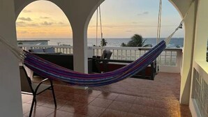 A hammock on a balcony with a view of the ocean and a sunset.