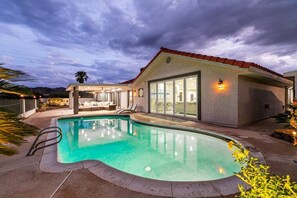 A modern house with a swimming pool, a patio with outdoor furniture, and a large glass door leading to a covered area.