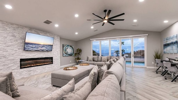 A modern living room with a fireplace, a large sofa, a dining area, and a view of the outdoors. - Stunning Lake View, Heated Pool, Single Story! (Boulder City)