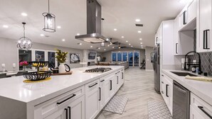 A modern kitchen with white cabinetry, a central island, stainless steel appliances, pendant lighting, and a ceiling fan. - Stunning Lake View, Heated Pool, Single Story! (Boulder City)