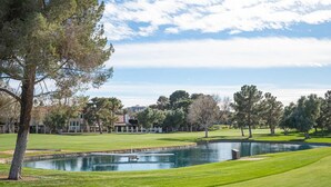 A golf course with a pond, trees, and a building in the background. - Gated- LV Country Club Sleeps 8 (Las Vegas)