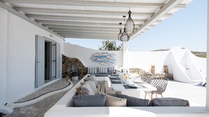 An outdoor seating area with a stone wall, a white ceiling, and a view of the landscape. - 3-bed Villa in Mykonos With Private Pool (Mykonos)