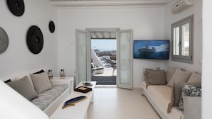 A modern living room with a sofa, a coffee table, and a TV. There are decorative plates on the wall and a view of the outside through a glass door. - 3-bed Villa in Mykonos With Private Pool (Mykonos)