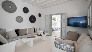 A modern living room with a white sofa, a coffee table, and a television mounted on the wall. - 3-bed Villa in Mykonos With Private Pool (Mykonos)