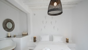 A modern hotel room with a bed, white walls, a round mirror, a white chair, and a hanging light fixture. - 3-bed Villa in Mykonos With Private Pool (Mykonos)