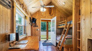 A cozy cabin with a wooden interior, a dining table, a bunk bed, and a ceiling fan. - Trapper cabin (Northport)