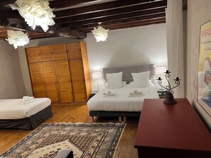 Un dormitorio con una cama, un armario de madera, una mesita de noche con un candelabro y una alfombra estampada.