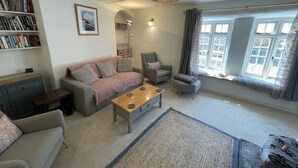 A living room with a sofa, armchairs, a coffee table, a bookshelf, and a large window with curtains. - The Brewhouse Boscastle Harbour (Boscastle)