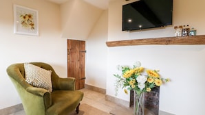 Una sala de estar con un sillón verde, una chimenea con un jarrón de flores, una puerta de madera y un televisor montado en la pared.