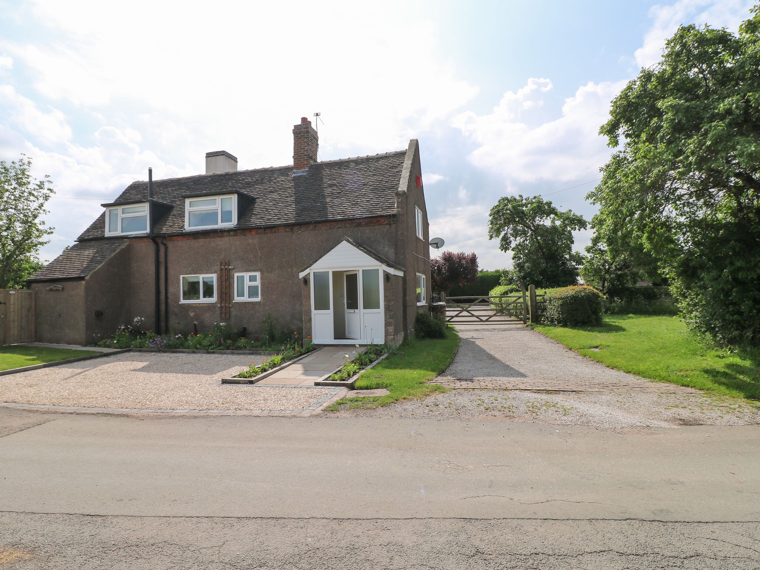 A two-story house with a front garden, a driveway, and a gated entrance.