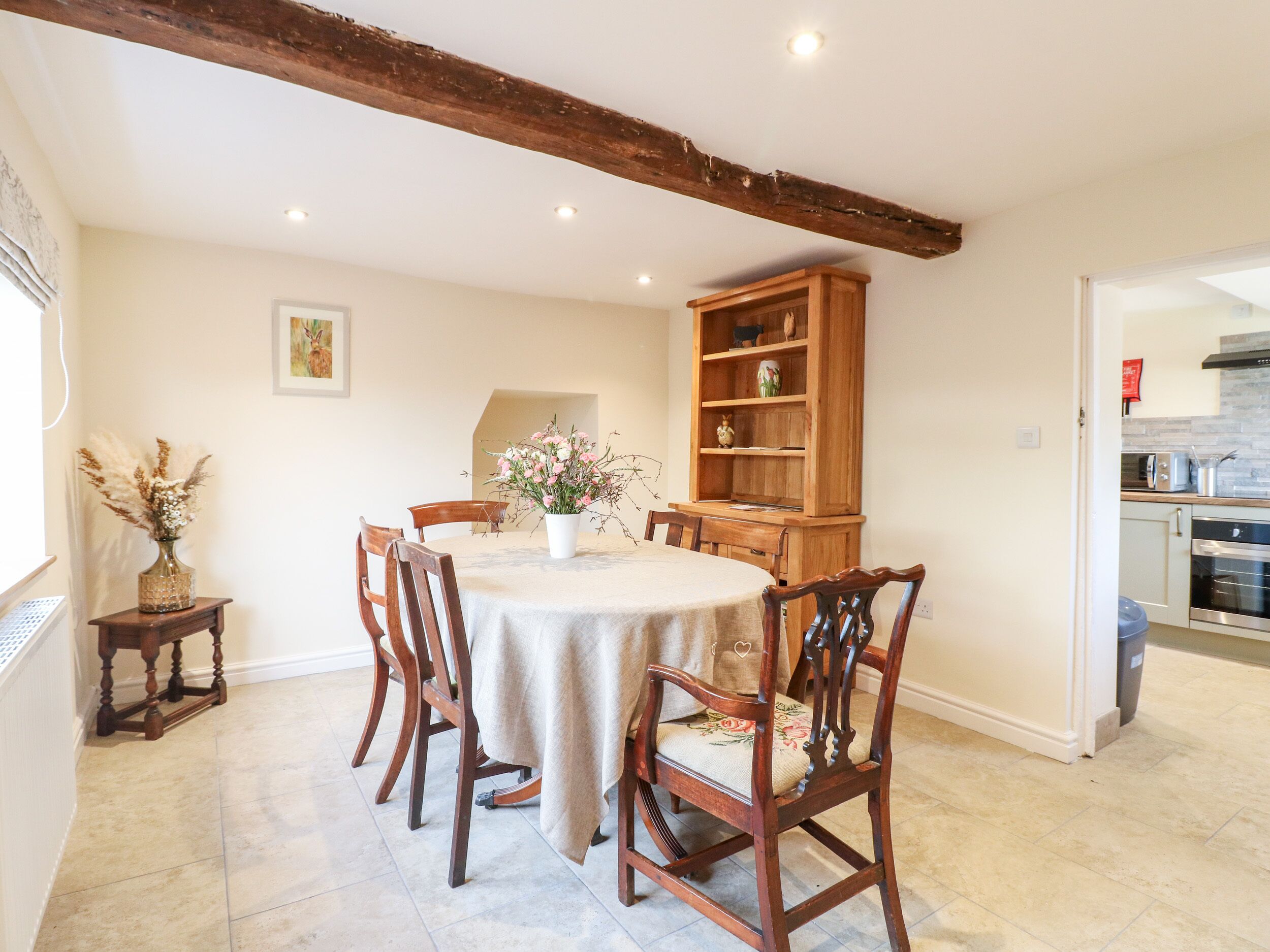 Un coin repas avec une table ronde, des chaises en bois, un buffet et un vase rempli de fleurs.