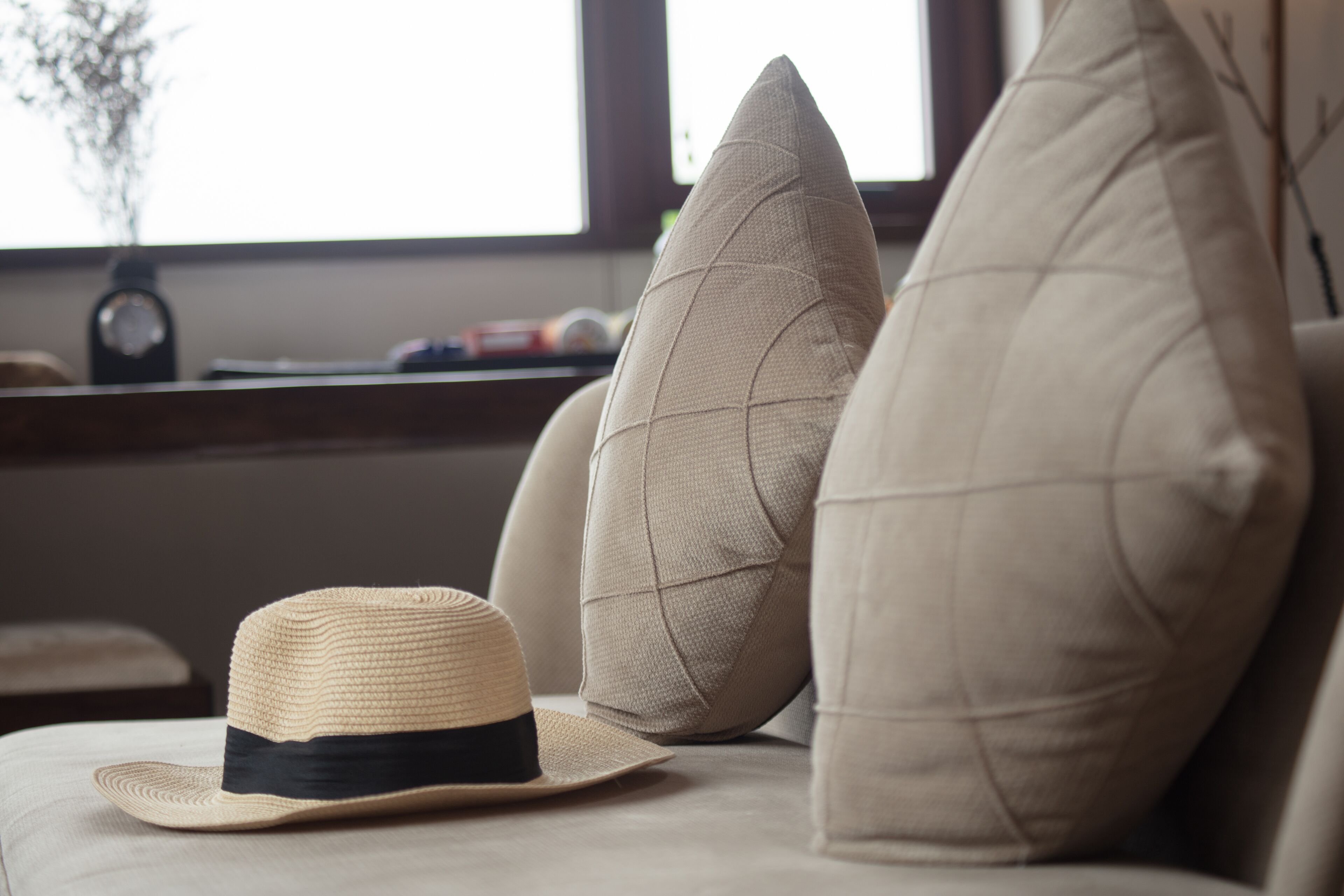 Un sombrero sobre un sofá, con una ventana y almohadas al fondo.