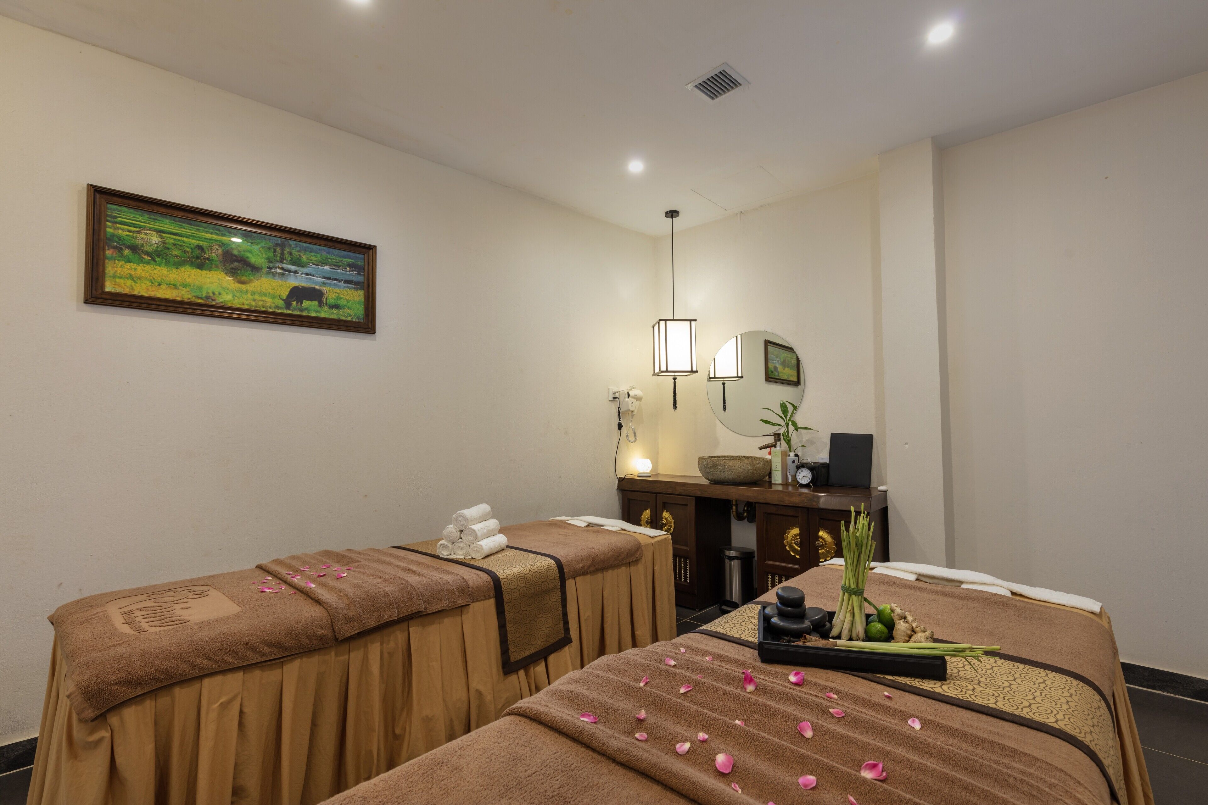 A room with two massage tables, a painting on the wall, a desk with a computer, and a plant.