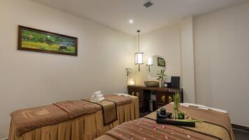 A room with two massage tables, a painting on the wall, a desk with a computer, and a plant.