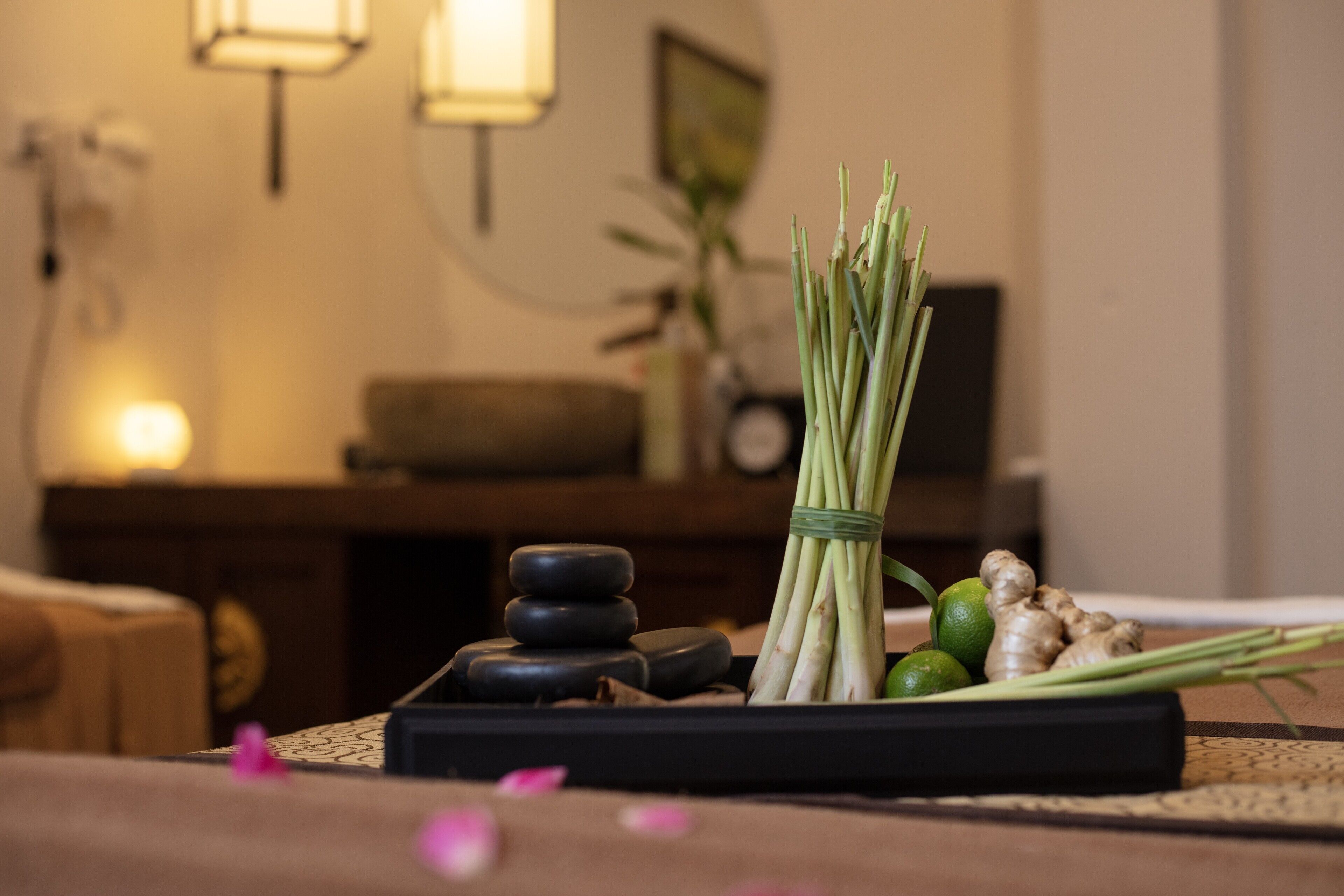 A room with a massage table, a small table with massage stones, a plant, and a lamp.