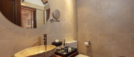 A bathroom with a stone sink, a round mirror, a toilet, and a wooden vanity.