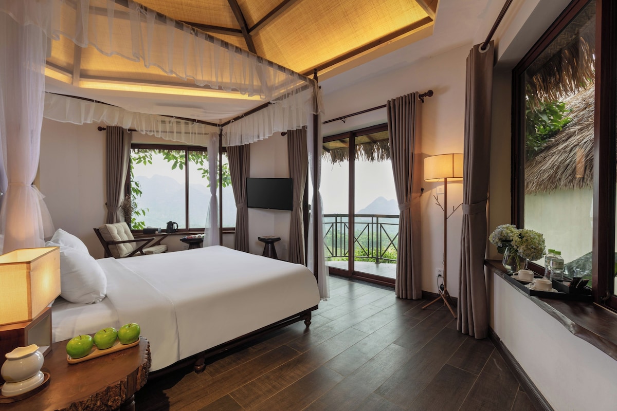 A hotel room with a bed, a TV, a balcony with a view, and a dining area.