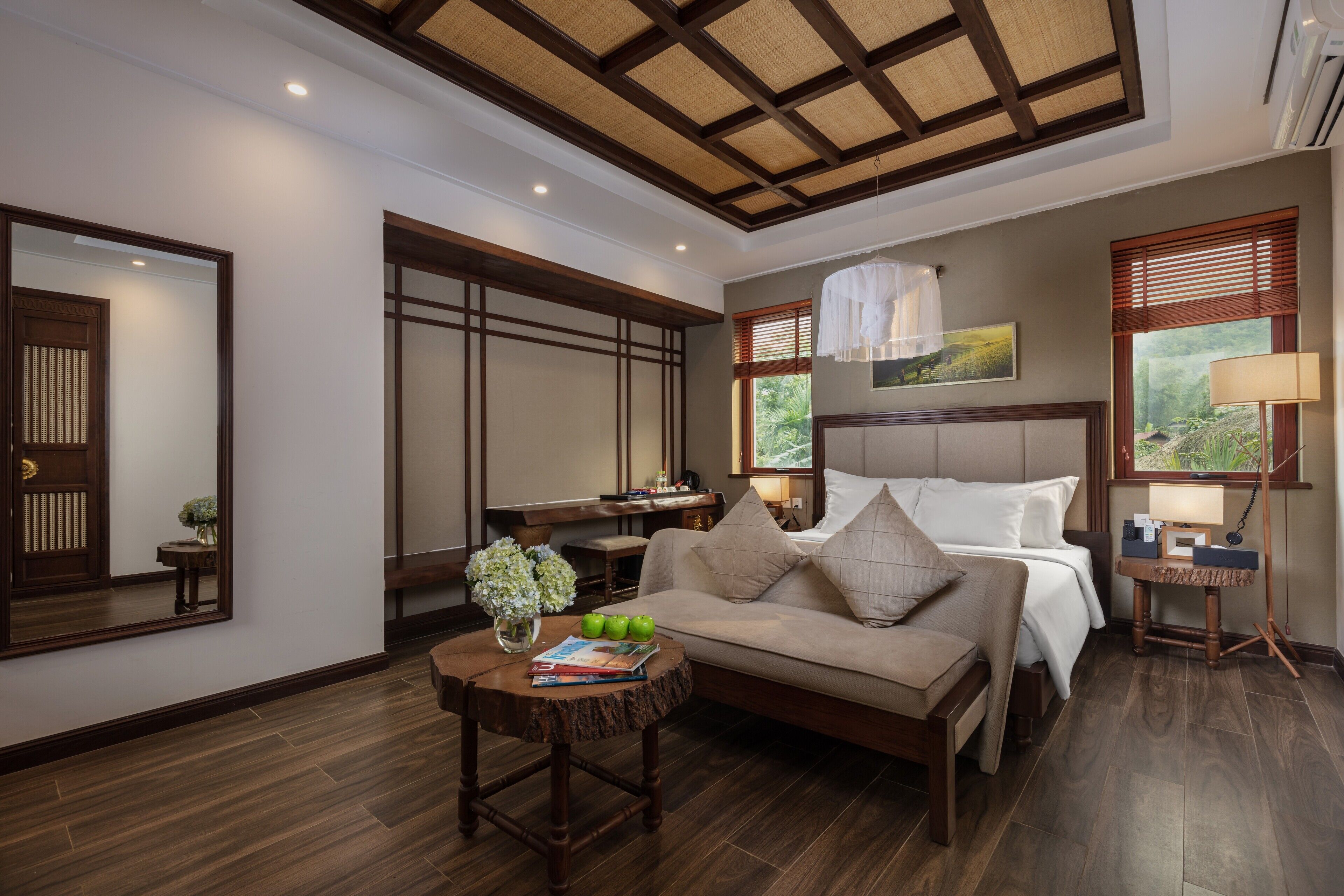 A well-lit bedroom with a large bed, a desk, and a seating area with a coffee table.