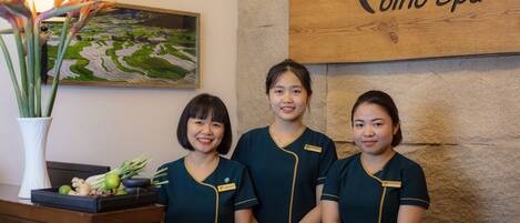 Three individuals in uniform standing in front of a reception desk with a wooden sign that reads "Cino Spa".