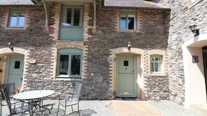 A stone building with a patio area featuring a round table and chairs. - Grade II Old Engine House, on the SW Coast Path (Noss Mayo)
