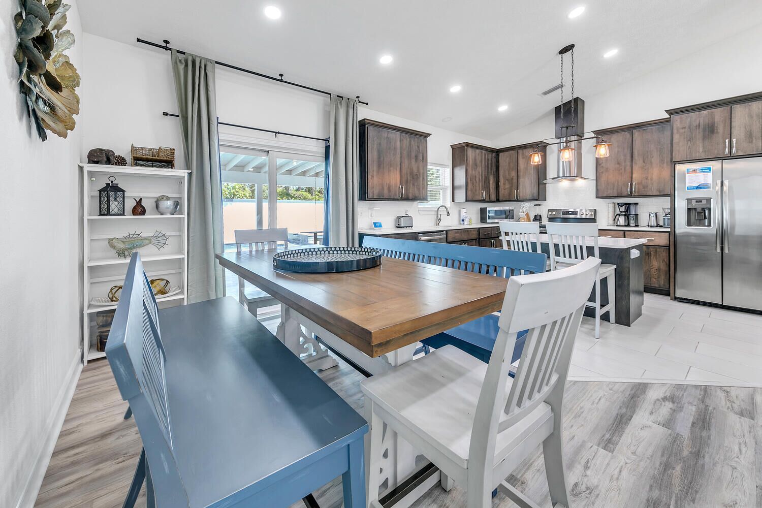 A modern kitchen with dark wood cabinets, a stainless steel refrigerator, and a dining area with blue chairs and a wooden table.