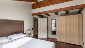 Quarto com uma cama grande, vigas de madeira, um guarda-roupa e uma porta que dá para outro cômodo.